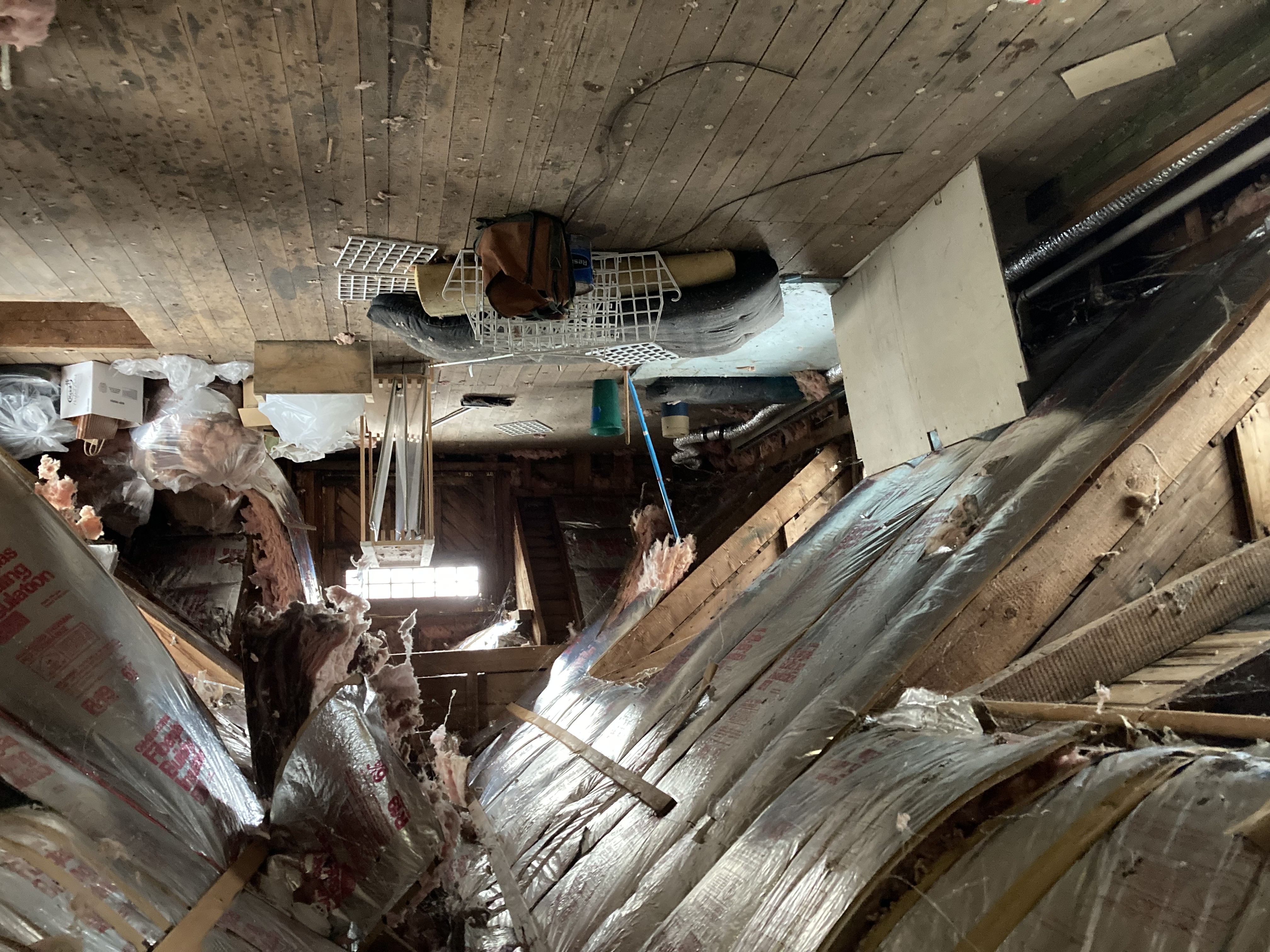 Image of Carriage's attic before improvements were made with stuff strewn about the floor and fiberglass batts coming out of the roof cavities