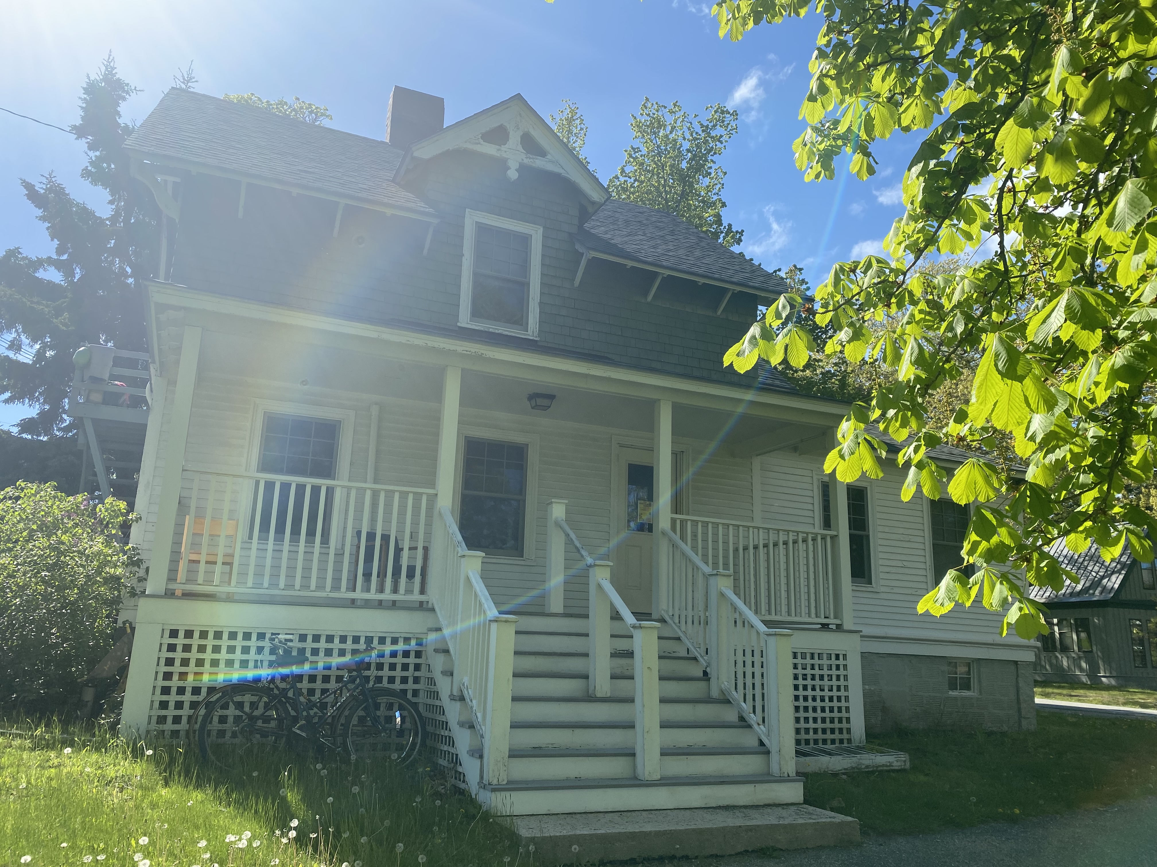 Small, white, two story house with a raised stone foundation and a large fenced and covered porch.